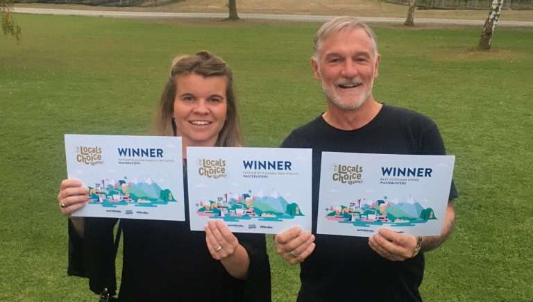 Smiling man and woman hold up three awards certificates which say: winner Wastebusters - Best clothing shop, Favourite sustainability initiative, Favourite Wānaka nonprofit