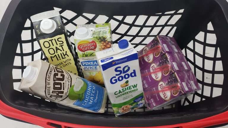 Black shopping basket filled with drinks packaged in liquid paperboard, e.g. oat milk and juice