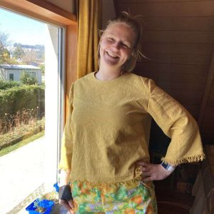 Sustainable designer Jessie smiling happily next to a big bright window while wearing her beautiful, colourful designs.