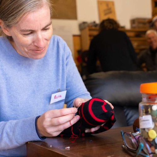 Ruth darning a sock with a smile